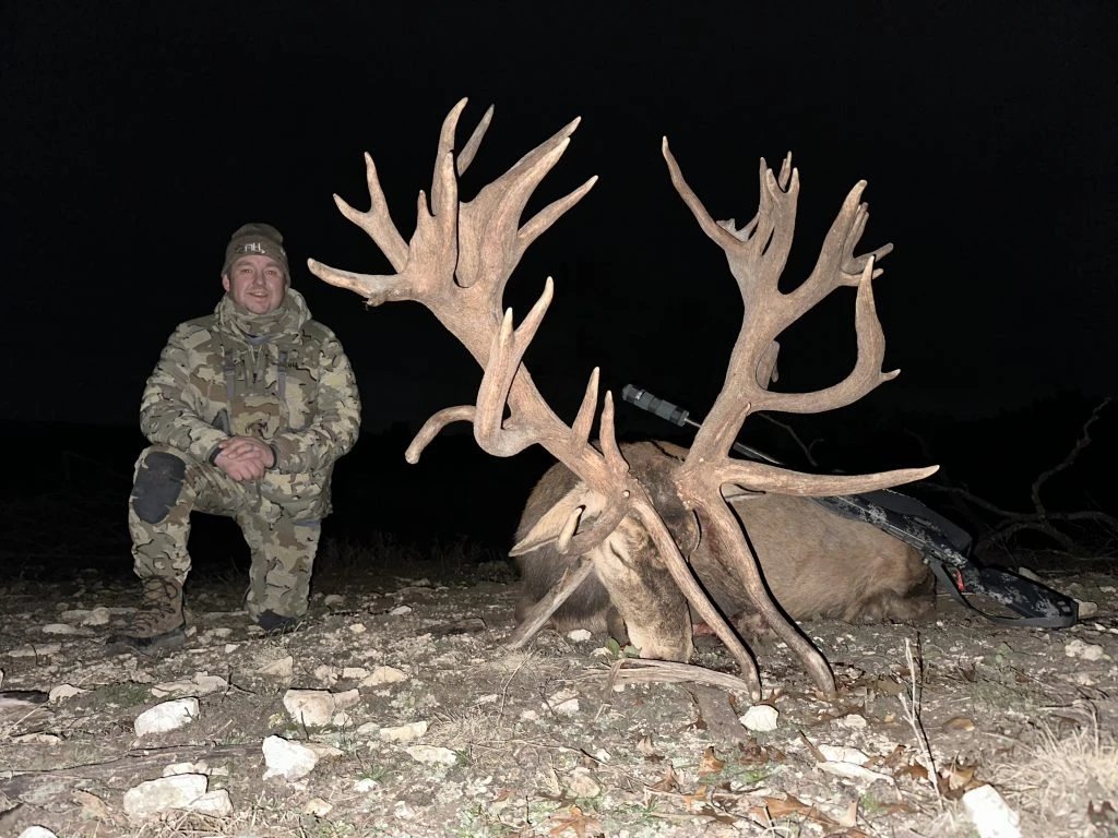 Hunter kneeling next to an enormous red stag taken on a evening hunt