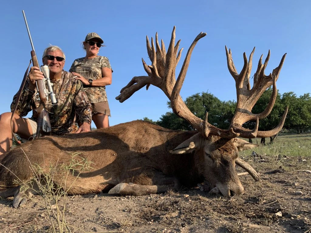 Hunter in camo standing next to a world-class red stag in grassy field